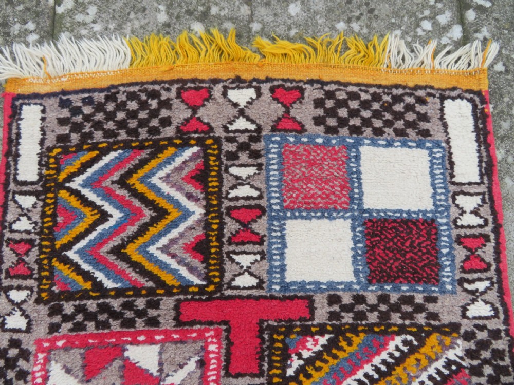 A rectangular hand-knotted Moroccan Berber wool rug featuring geometric patchwork panels in pink, yellow, black, grey, and white with fringed ends. View III