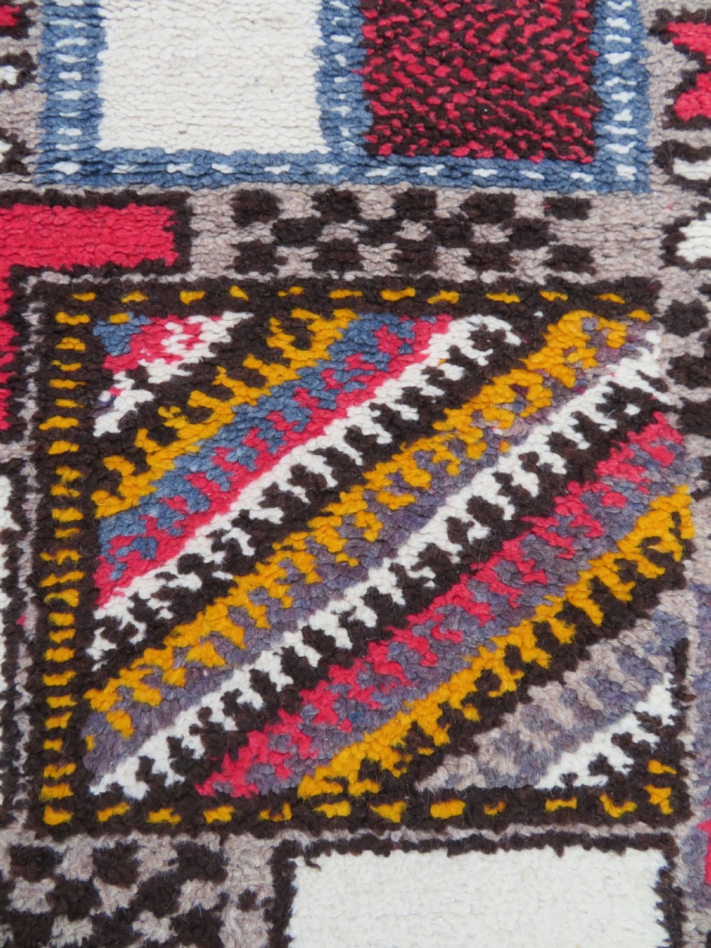 A rectangular hand-knotted Moroccan Berber wool rug featuring geometric patchwork panels in pink, yellow, black, grey, and white with fringed ends. View V
