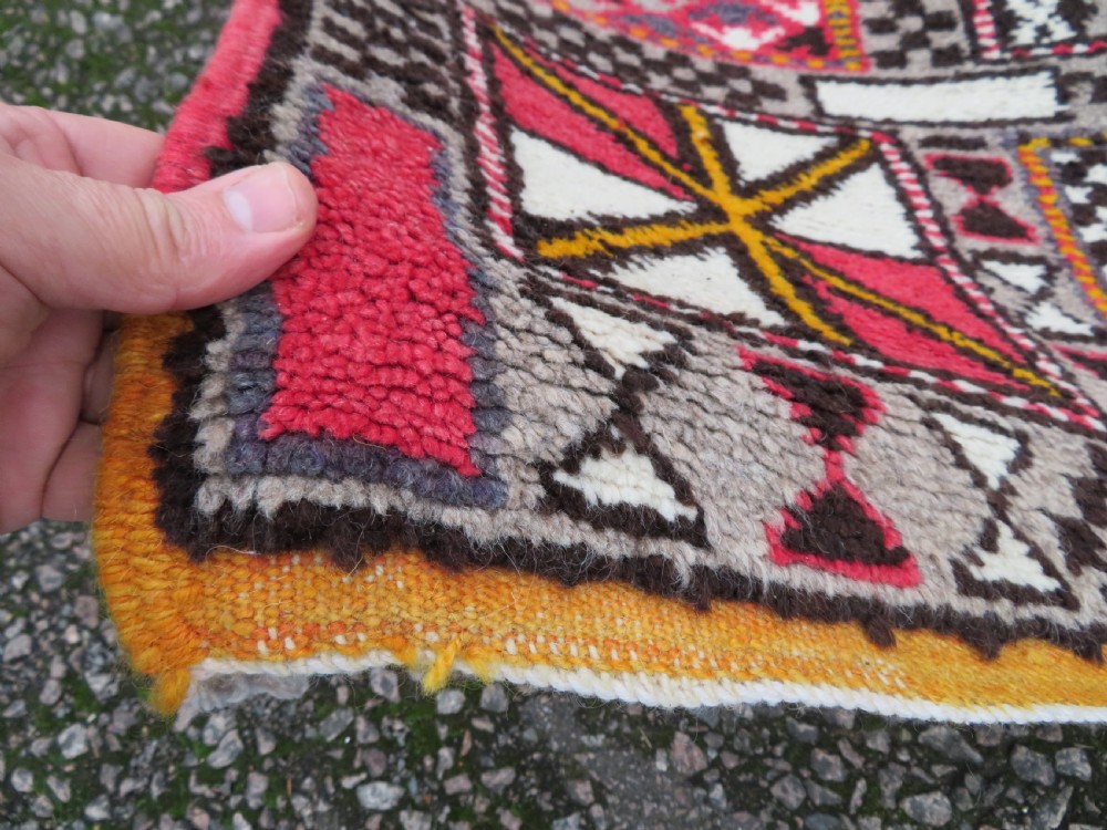 A rectangular hand-knotted Moroccan Berber wool rug featuring geometric patchwork panels in pink, yellow, black, grey, and white with fringed ends. View VII