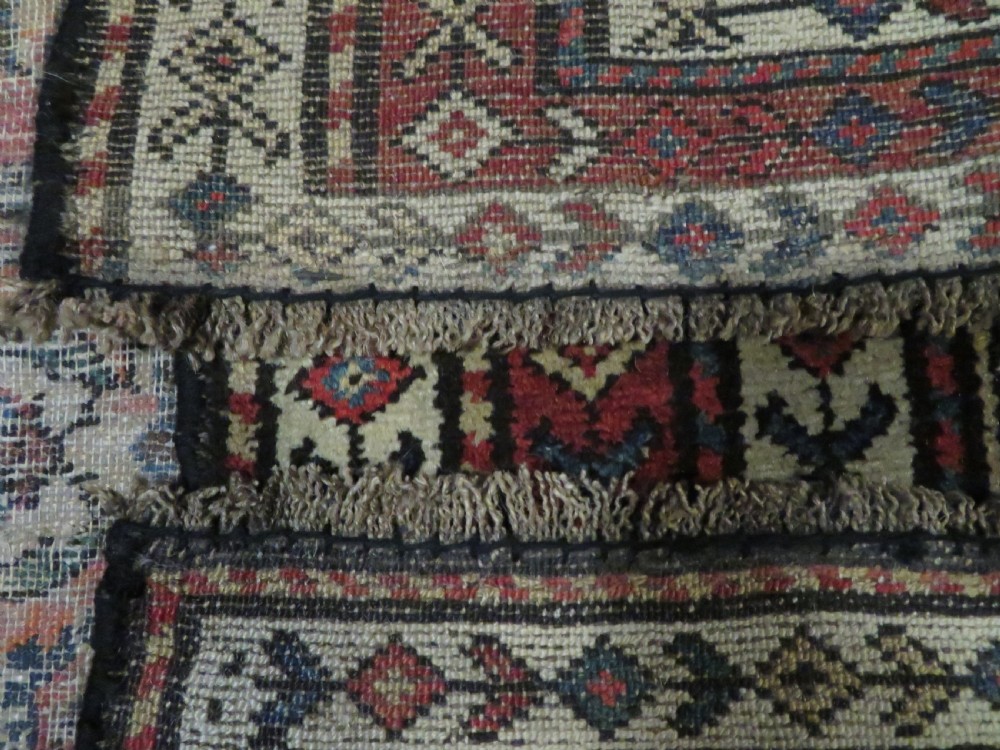 A long hand-knotted antique Kurdish Kelleh wool rug featuring geometric diamond medallions in red and navy blue on a dark brown field with patterned borders. View XIX