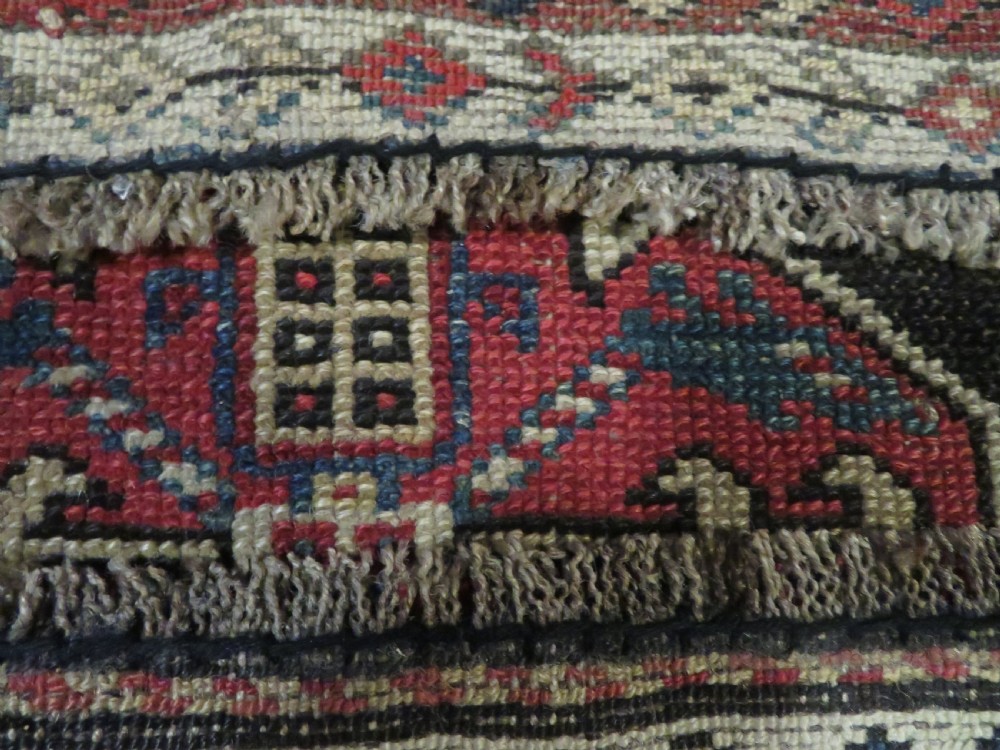 A long hand-knotted antique Kurdish Kelleh wool rug featuring geometric diamond medallions in red and navy blue on a dark brown field with patterned borders. View XX