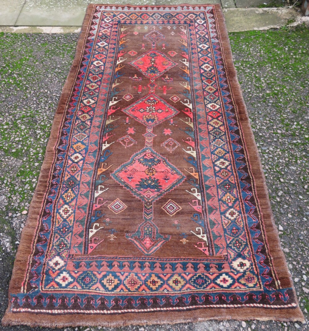 An antique Kurdish hand-knotted long wool rug featuring three central red diamond medallions surrounded by geometric tribal borders on a dark brown field.