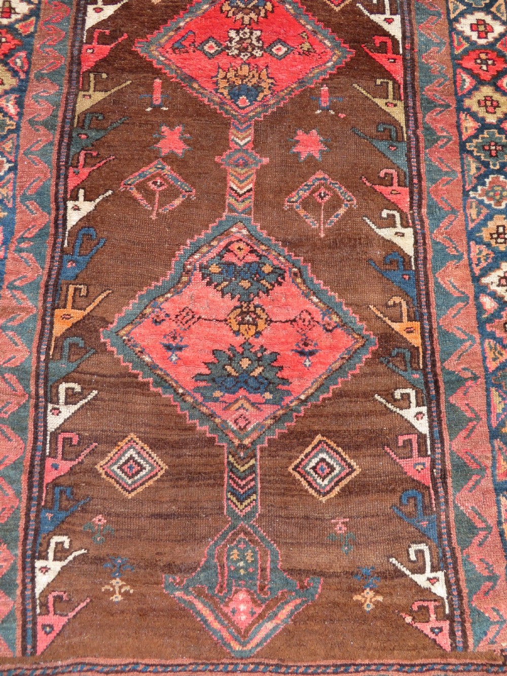 An antique Kurdish hand-knotted long wool rug featuring three central red diamond medallions surrounded by geometric tribal borders on a dark brown field. View III