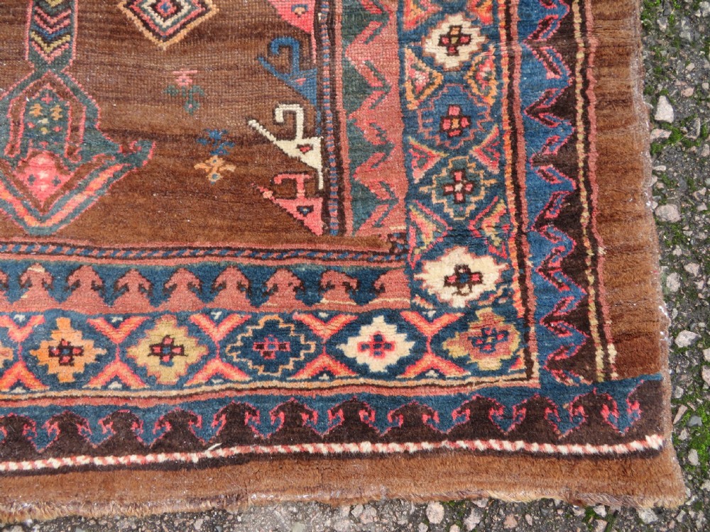 An antique Kurdish hand-knotted long wool rug featuring three central red diamond medallions surrounded by geometric tribal borders on a dark brown field. View X