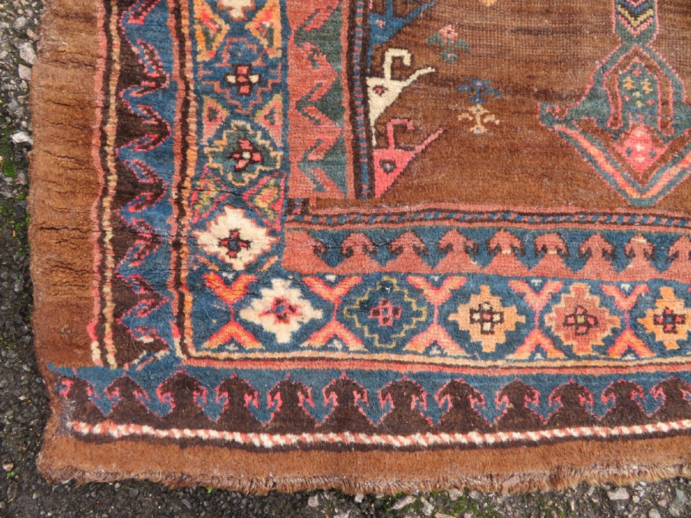 An antique Kurdish hand-knotted long wool rug featuring three central red diamond medallions surrounded by geometric tribal borders on a dark brown field. View XI
