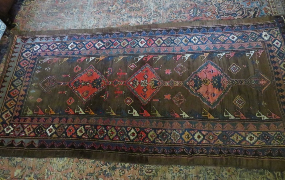 An antique Kurdish hand-knotted long wool rug featuring three central red diamond medallions surrounded by geometric tribal borders on a dark brown field. View XVIII