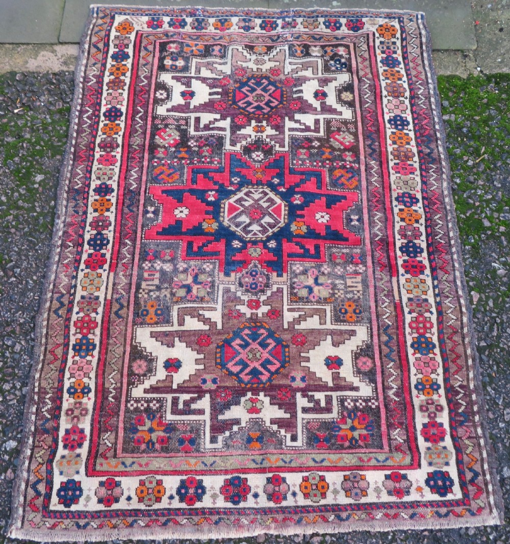 An antique hand-knotted Caucasian Lesghi wool rug featuring geometric star medallions in red, blue, cream, and brown surrounded by decorative pattern borders.