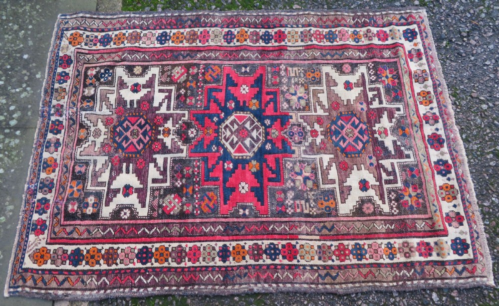 An antique hand-knotted Caucasian Lesghi wool rug featuring geometric star medallions in red, blue, cream, and brown surrounded by decorative pattern borders. View II