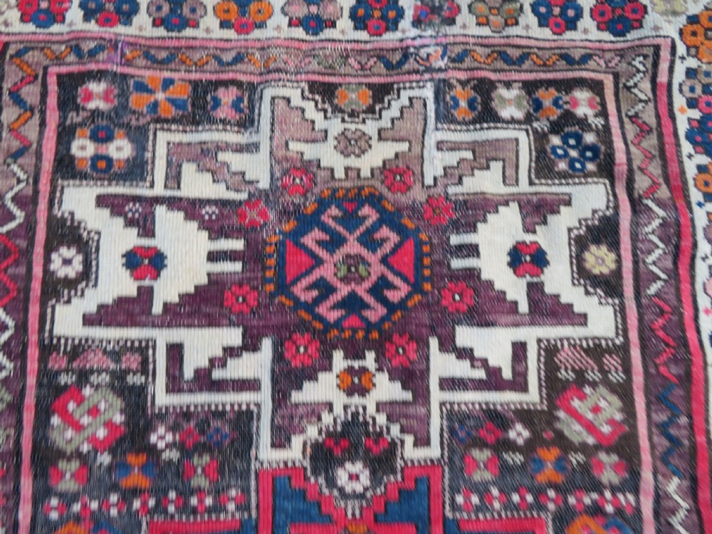 An antique hand-knotted Caucasian Lesghi wool rug featuring geometric star medallions in red, blue, cream, and brown surrounded by decorative pattern borders. View III