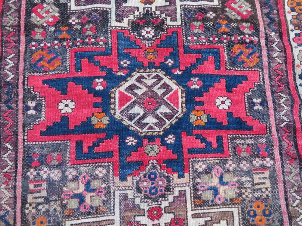 An antique hand-knotted Caucasian Lesghi wool rug featuring geometric star medallions in red, blue, cream, and brown surrounded by decorative pattern borders. View IV
