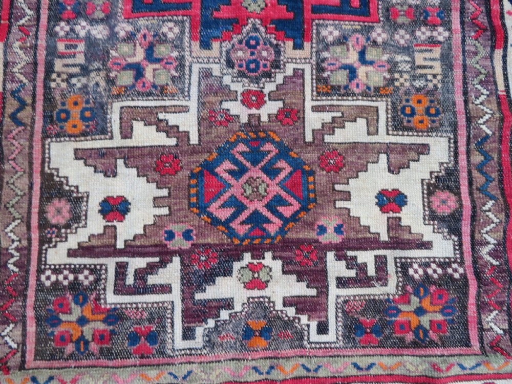 An antique hand-knotted Caucasian Lesghi wool rug featuring geometric star medallions in red, blue, cream, and brown surrounded by decorative pattern borders. View V
