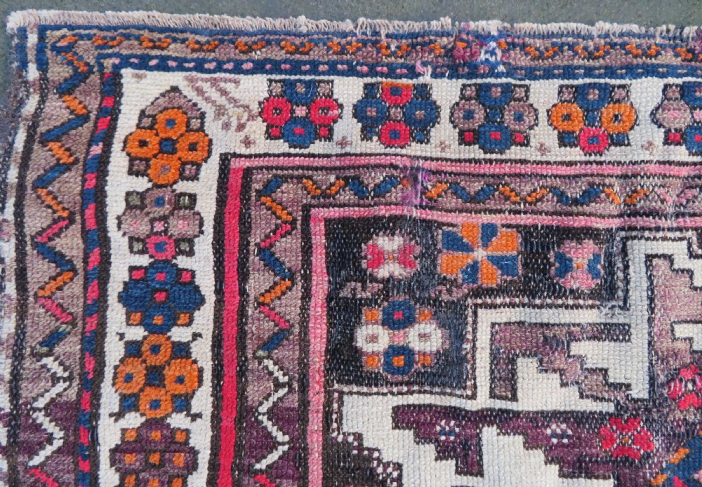 An antique hand-knotted Caucasian Lesghi wool rug featuring geometric star medallions in red, blue, cream, and brown surrounded by decorative pattern borders. View IX