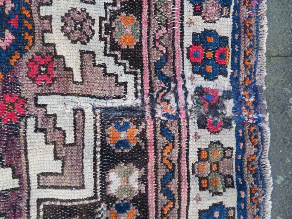 An antique hand-knotted Caucasian Lesghi wool rug featuring geometric star medallions in red, blue, cream, and brown surrounded by decorative pattern borders. View X