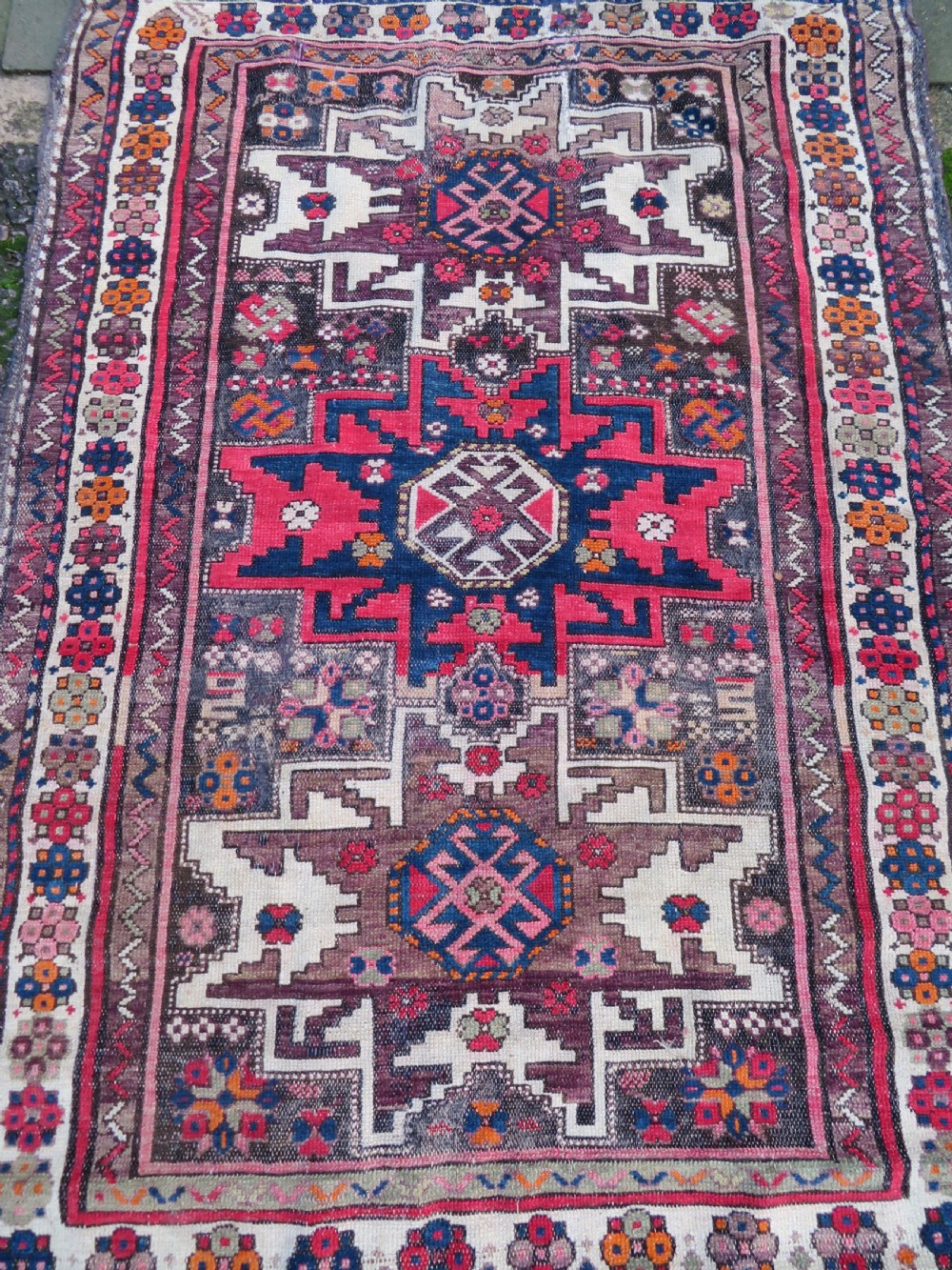 An antique hand-knotted Caucasian Lesghi wool rug featuring geometric star medallions in red, blue, cream, and brown surrounded by decorative pattern borders. View XIII