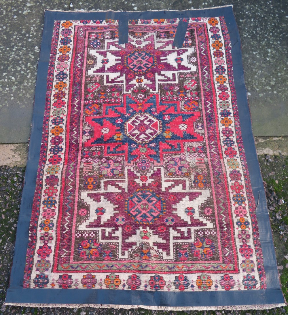 An antique hand-knotted Caucasian Lesghi wool rug featuring geometric star medallions in red, blue, cream, and brown surrounded by decorative pattern borders. View XIV