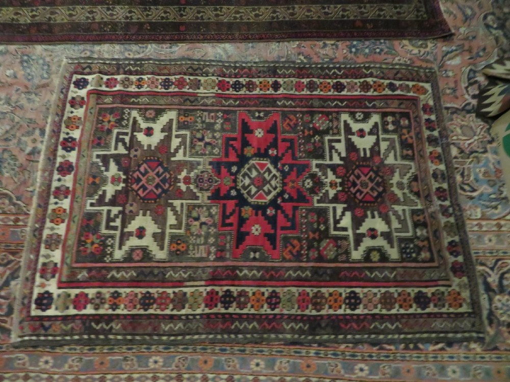 An antique hand-knotted Caucasian Lesghi wool rug featuring geometric star medallions in red, blue, cream, and brown surrounded by decorative pattern borders. View XIX