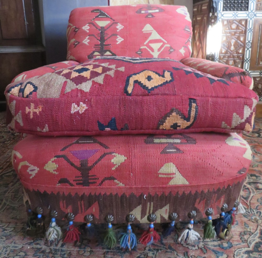 An antique low-slung club armchair upholstered in a geometric red wool kilim textile with turned legs and brass castors. View II