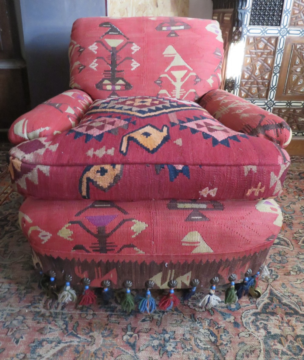 An antique low-slung club armchair upholstered in a geometric red wool kilim textile with turned legs and brass castors. View XXI