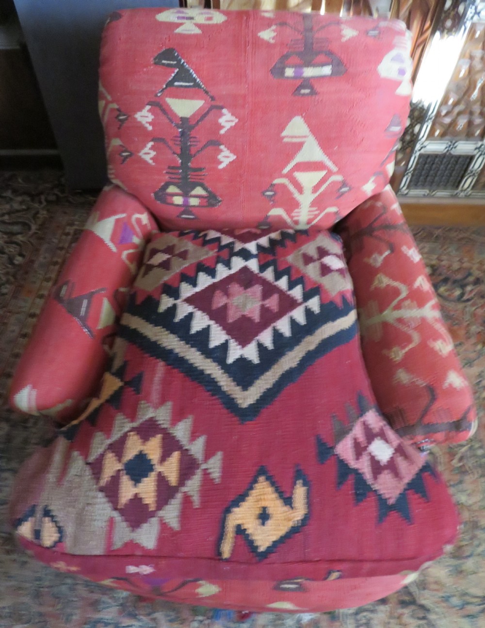 An antique low-slung club armchair upholstered in a geometric red wool kilim textile with turned legs and brass castors. View XXII