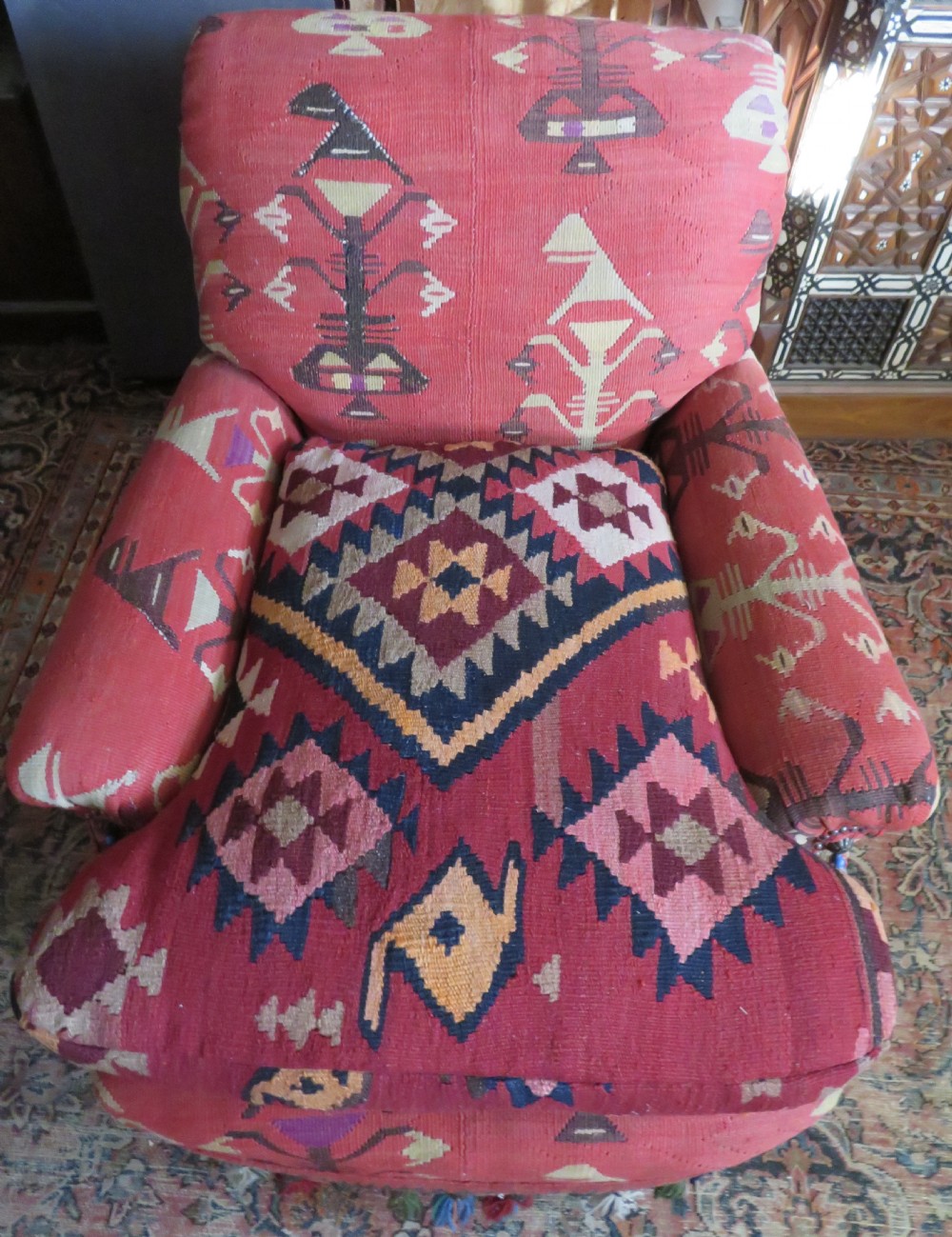 An antique low-slung club armchair upholstered in a geometric red wool kilim textile with turned legs and brass castors. View XXIII