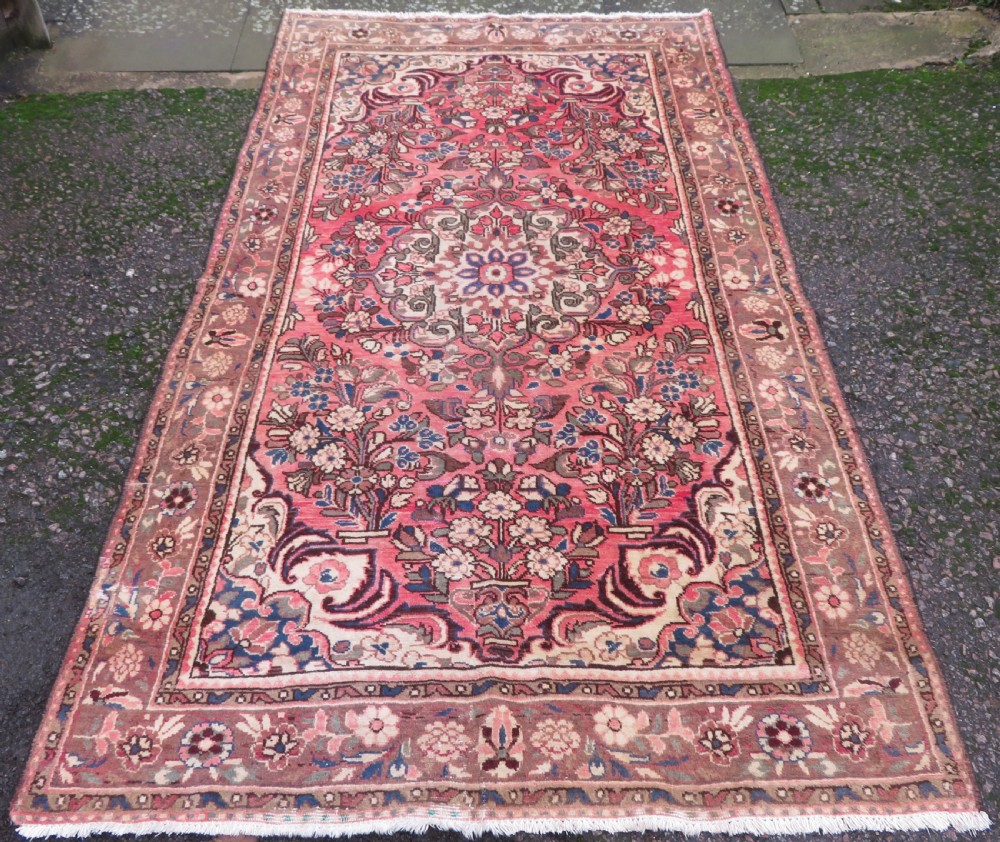 A large rectangular hand-knotted Persian Hamadan wool rug featuring a central floral medallion surrounded by intricate floral motifs in shades of rose pink, cream, brown, and blue.