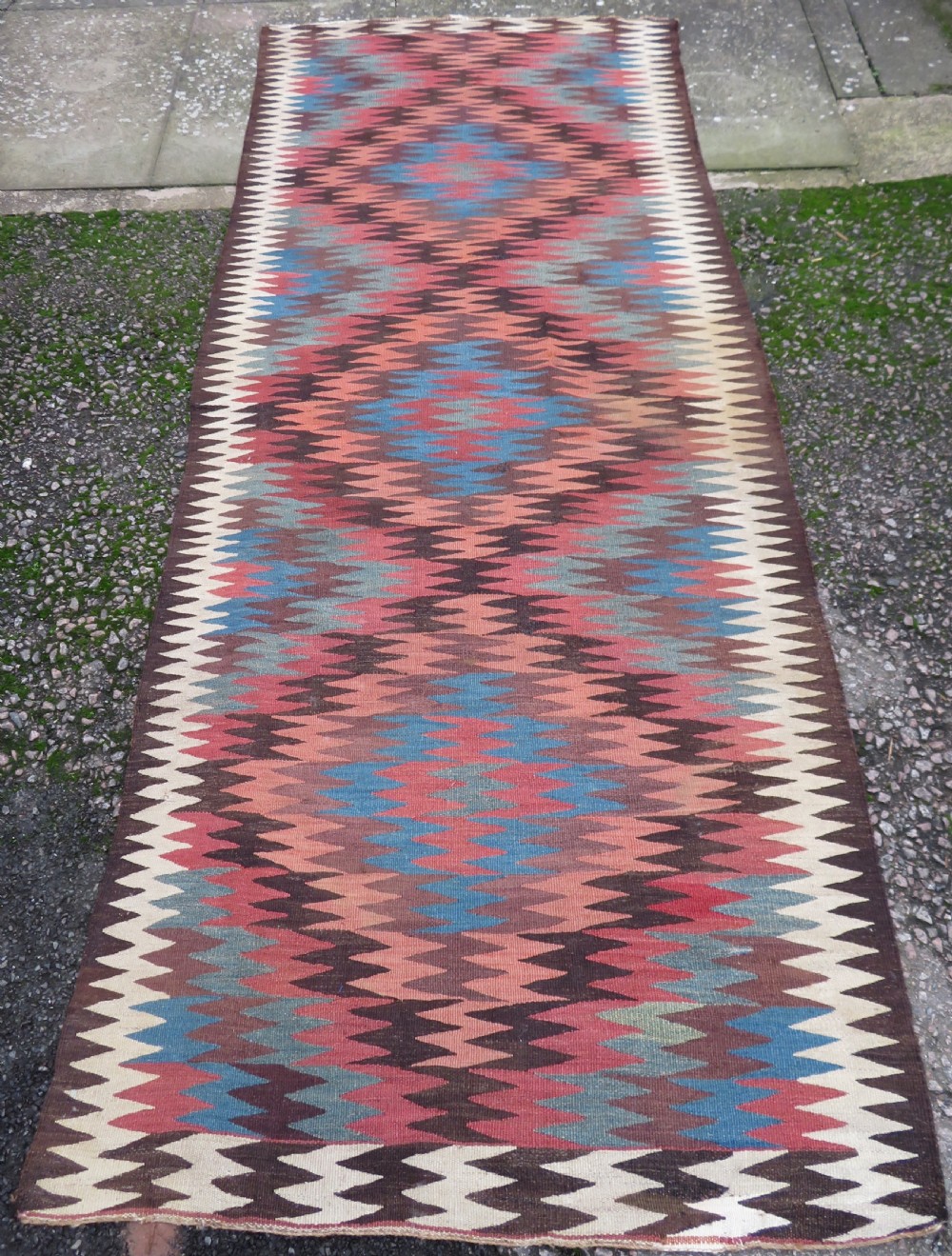 A long handwoven wool kilim runner displaying repeated serrated geometric diamond patterns in terracotta, blue, cream, and brown.