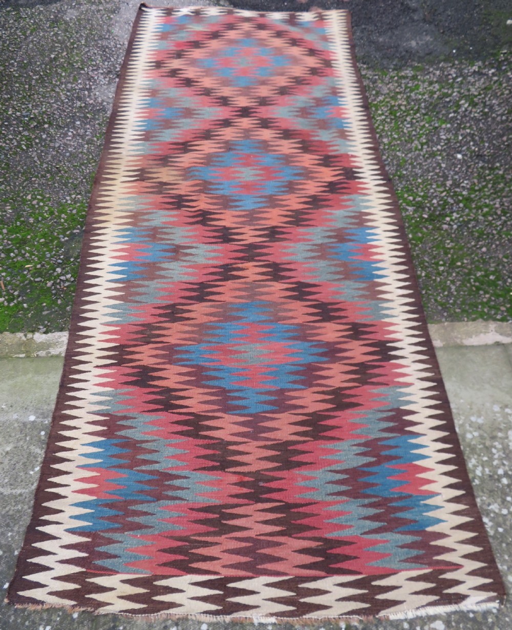 A long handwoven wool kilim runner displaying repeated serrated geometric diamond patterns in terracotta, blue, cream, and brown. View II