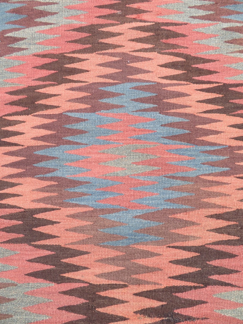 A long handwoven wool kilim runner displaying repeated serrated geometric diamond patterns in terracotta, blue, cream, and brown. View III