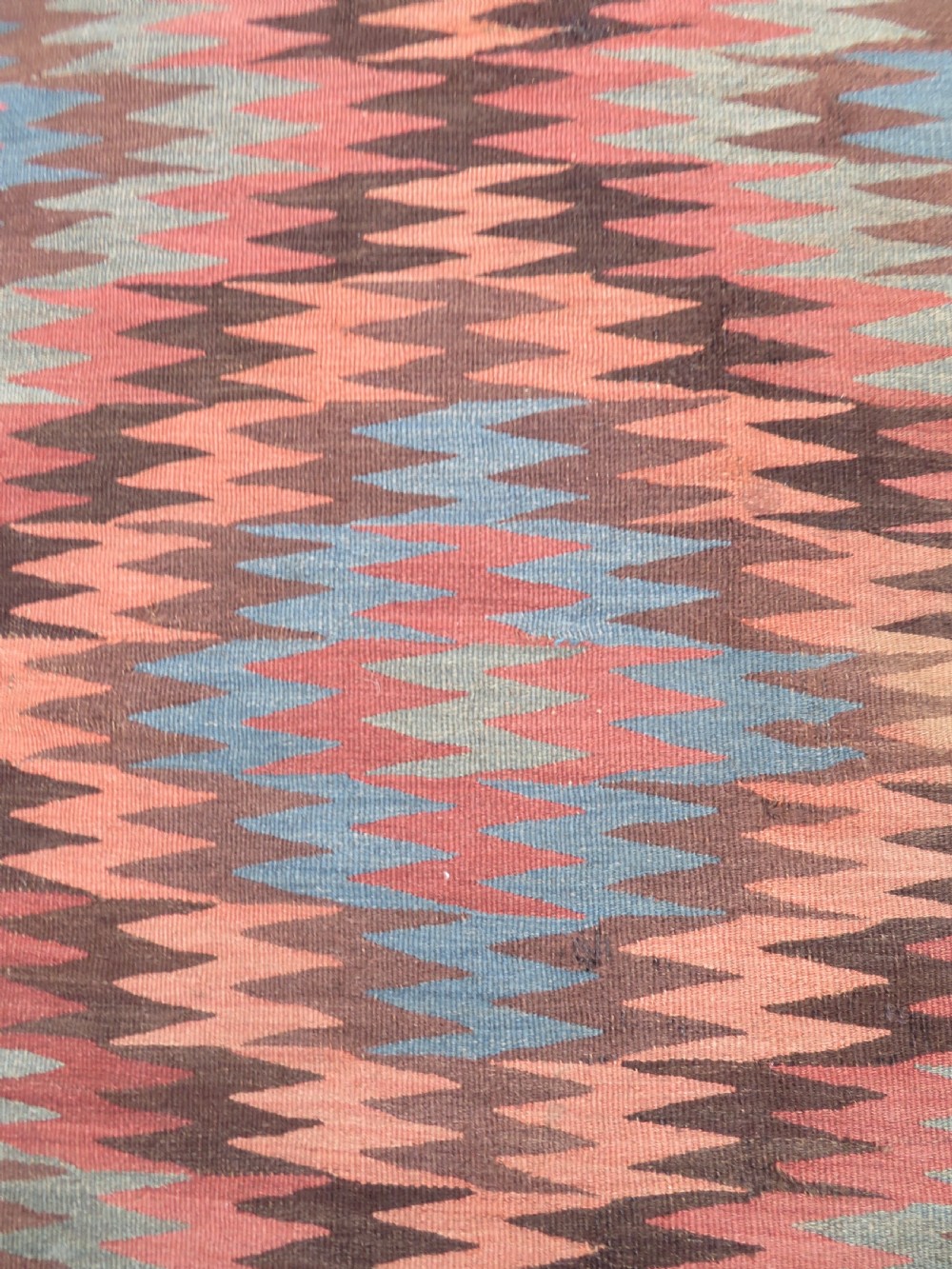A long handwoven wool kilim runner displaying repeated serrated geometric diamond patterns in terracotta, blue, cream, and brown. View IV