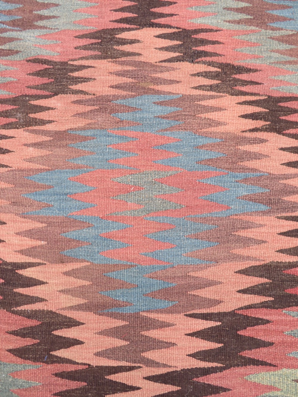 A long handwoven wool kilim runner displaying repeated serrated geometric diamond patterns in terracotta, blue, cream, and brown. View V