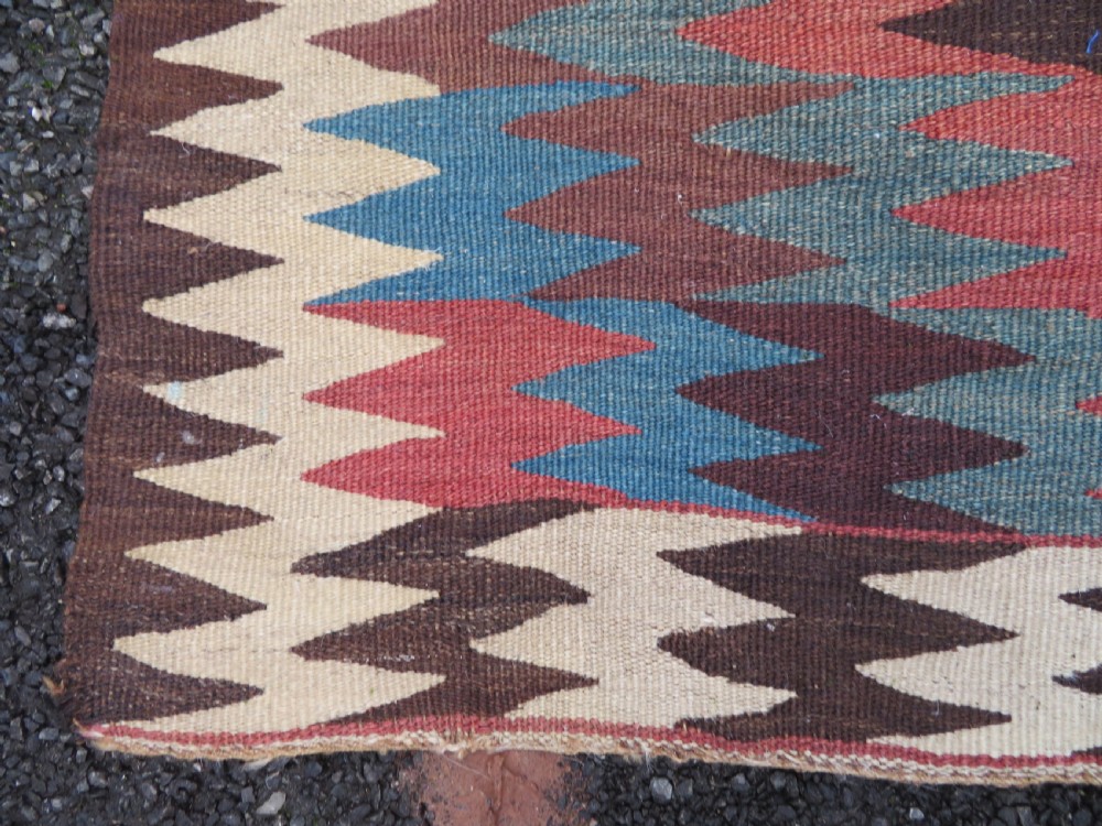 A long handwoven wool kilim runner displaying repeated serrated geometric diamond patterns in terracotta, blue, cream, and brown. View VI