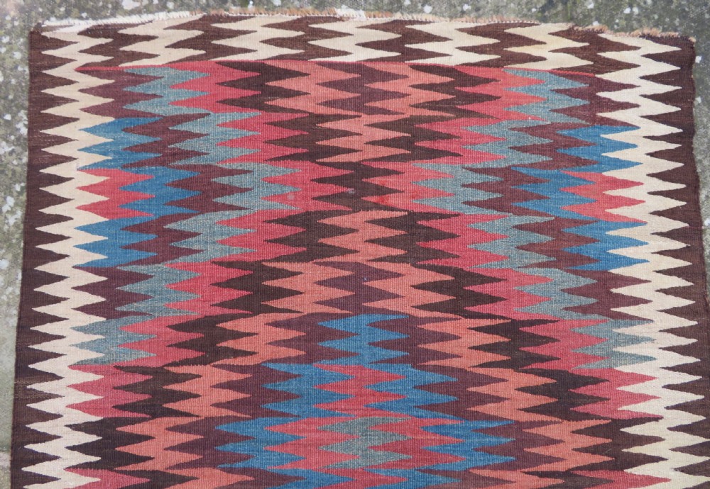 A long handwoven wool kilim runner displaying repeated serrated geometric diamond patterns in terracotta, blue, cream, and brown. View VII