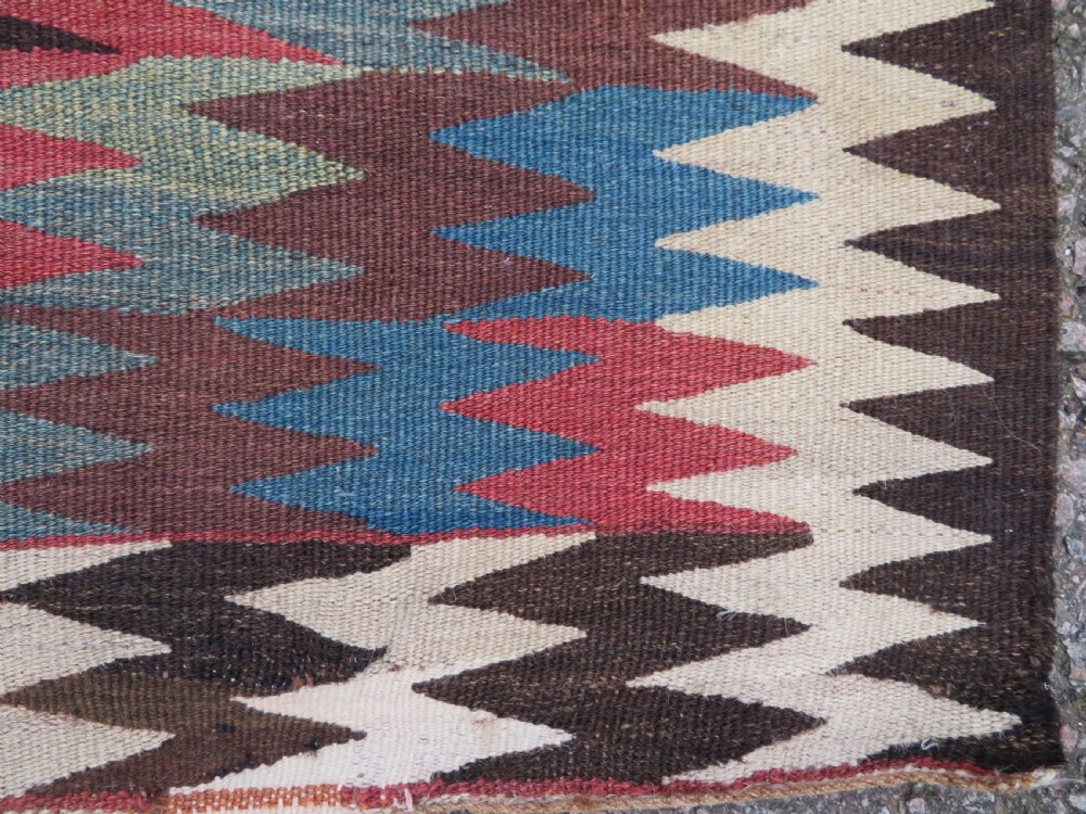 A long handwoven wool kilim runner displaying repeated serrated geometric diamond patterns in terracotta, blue, cream, and brown. View VIII