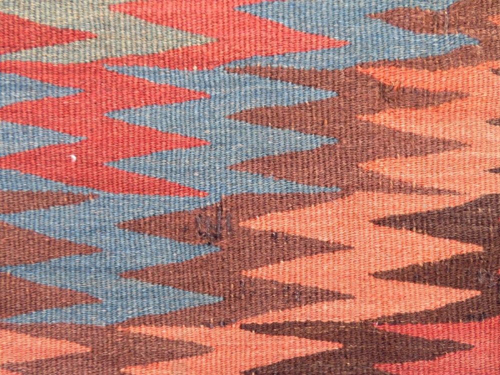 A long handwoven wool kilim runner displaying repeated serrated geometric diamond patterns in terracotta, blue, cream, and brown. View IX