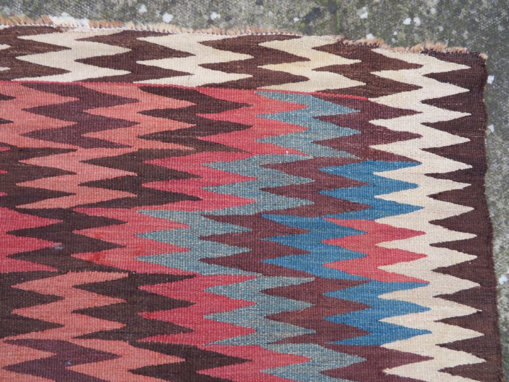 A long handwoven wool kilim runner displaying repeated serrated geometric diamond patterns in terracotta, blue, cream, and brown. View X