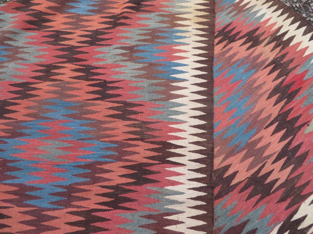 A long handwoven wool kilim runner displaying repeated serrated geometric diamond patterns in terracotta, blue, cream, and brown. View XII