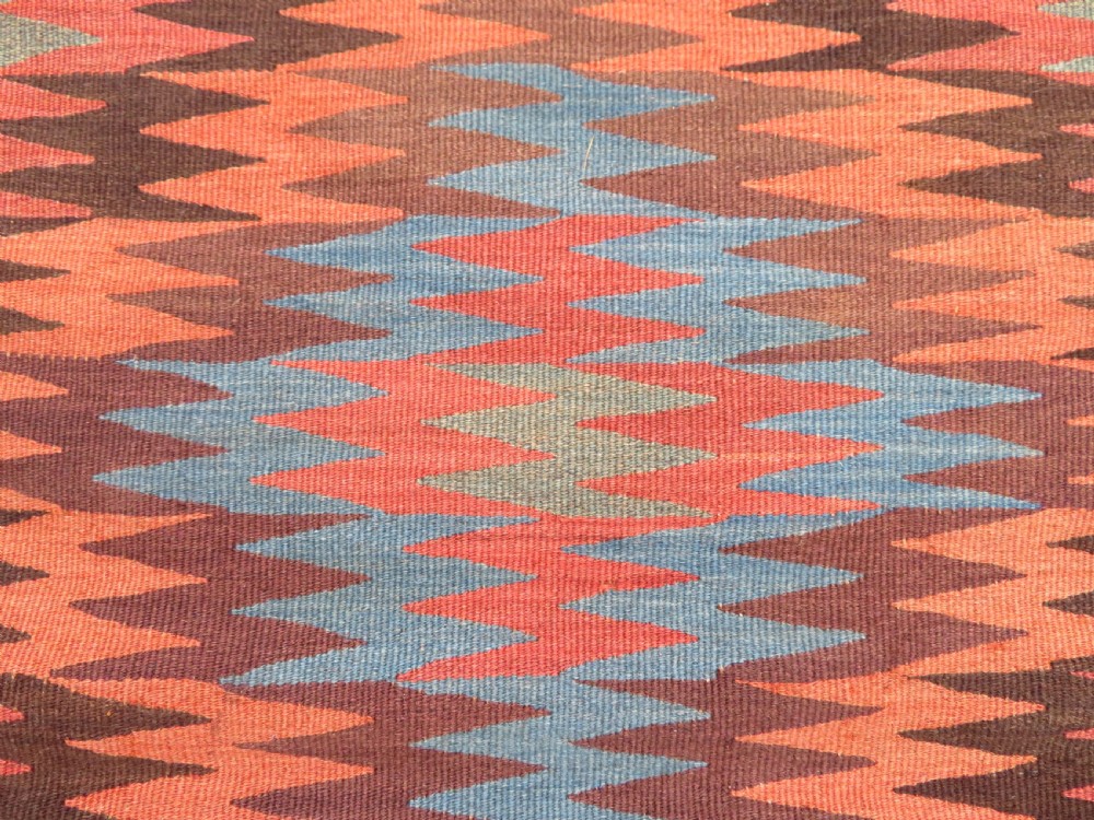 A long handwoven wool kilim runner displaying repeated serrated geometric diamond patterns in terracotta, blue, cream, and brown. View XIV