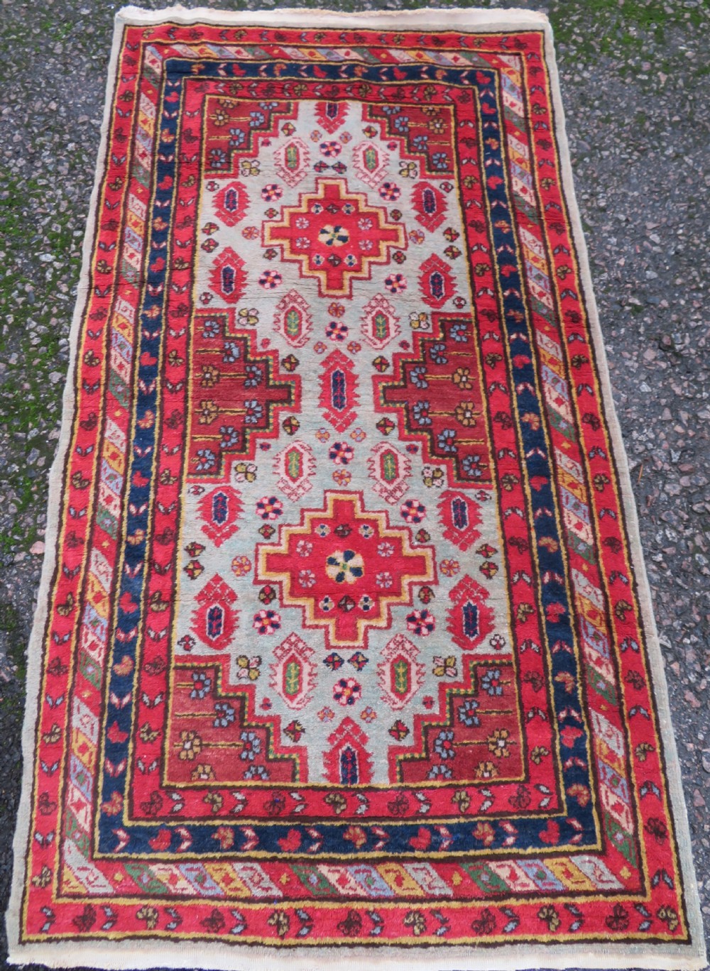 A hand-knotted Turkish village rug featuring central geometric stepped medallions in red, yellow, and navy on a cream field surrounded by decorative borders.