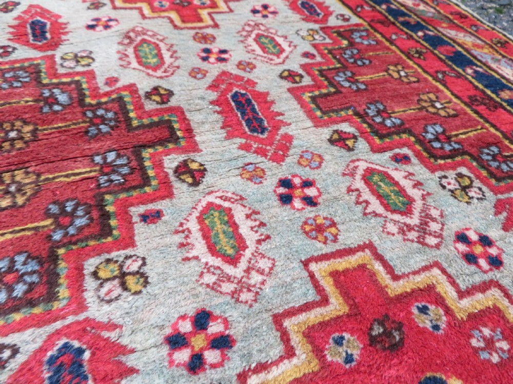 A hand-knotted Turkish village rug featuring central geometric stepped medallions in red, yellow, and navy on a cream field surrounded by decorative borders. View VI