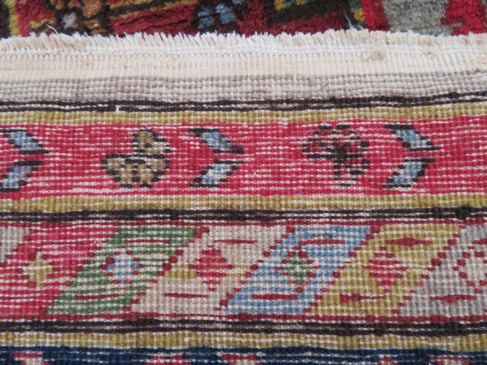 A hand-knotted Turkish village rug featuring central geometric stepped medallions in red, yellow, and navy on a cream field surrounded by decorative borders. View IX