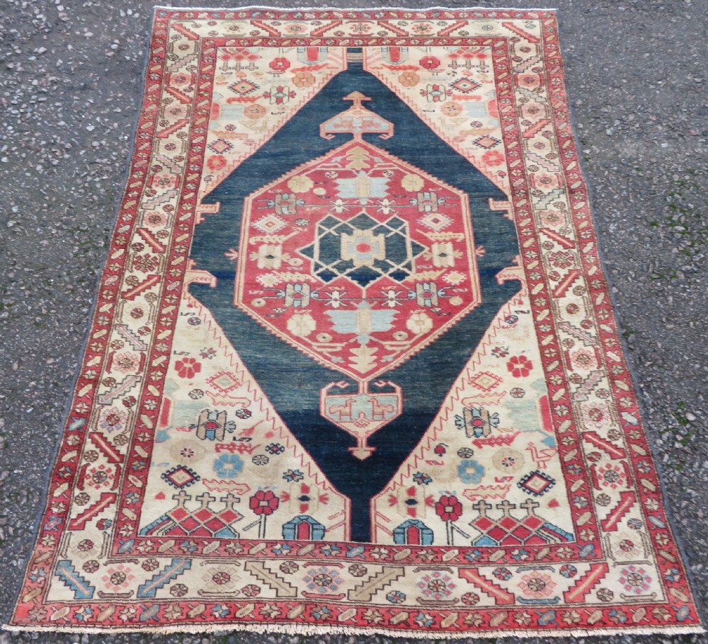 An antique Bakshaish hand-knotted wool rug featuring a navy blue and terracotta central geometric medallion on a cream field with patterned borders.