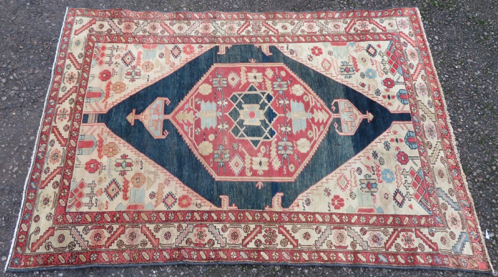 An antique Bakshaish hand-knotted wool rug featuring a navy blue and terracotta central geometric medallion on a cream field with patterned borders. View II