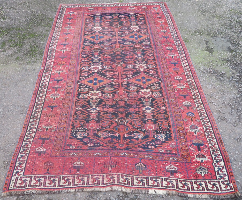 A large hand-knotted Persian Bakhtiari rug featuring geometric diamond medallions on a dark navy field surrounded by a detailed red patterned border.