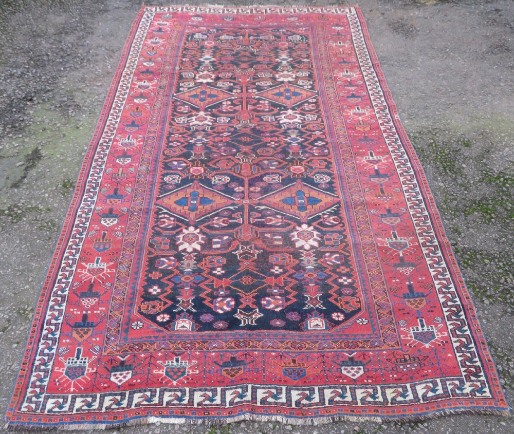 A large hand-knotted Persian Bakhtiari rug featuring geometric diamond medallions on a dark navy field surrounded by a detailed red patterned border. View II