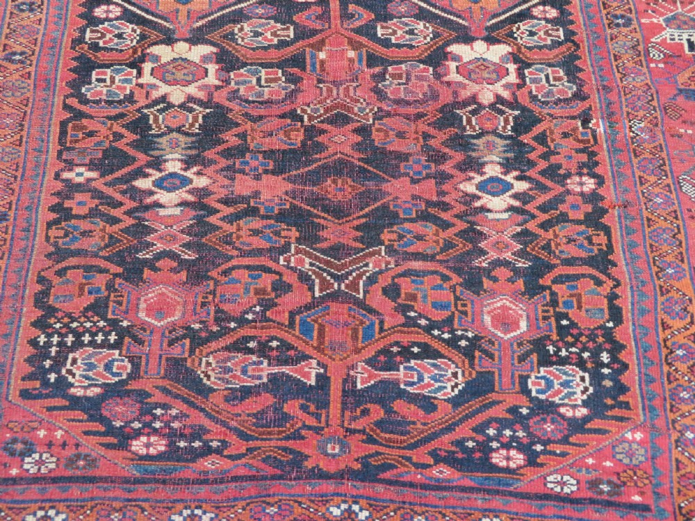 A large hand-knotted Persian Bakhtiari rug featuring geometric diamond medallions on a dark navy field surrounded by a detailed red patterned border. View III