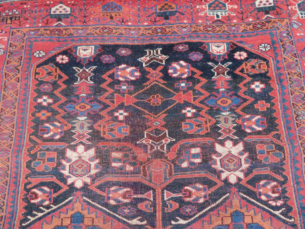 A large hand-knotted Persian Bakhtiari rug featuring geometric diamond medallions on a dark navy field surrounded by a detailed red patterned border. View VIII