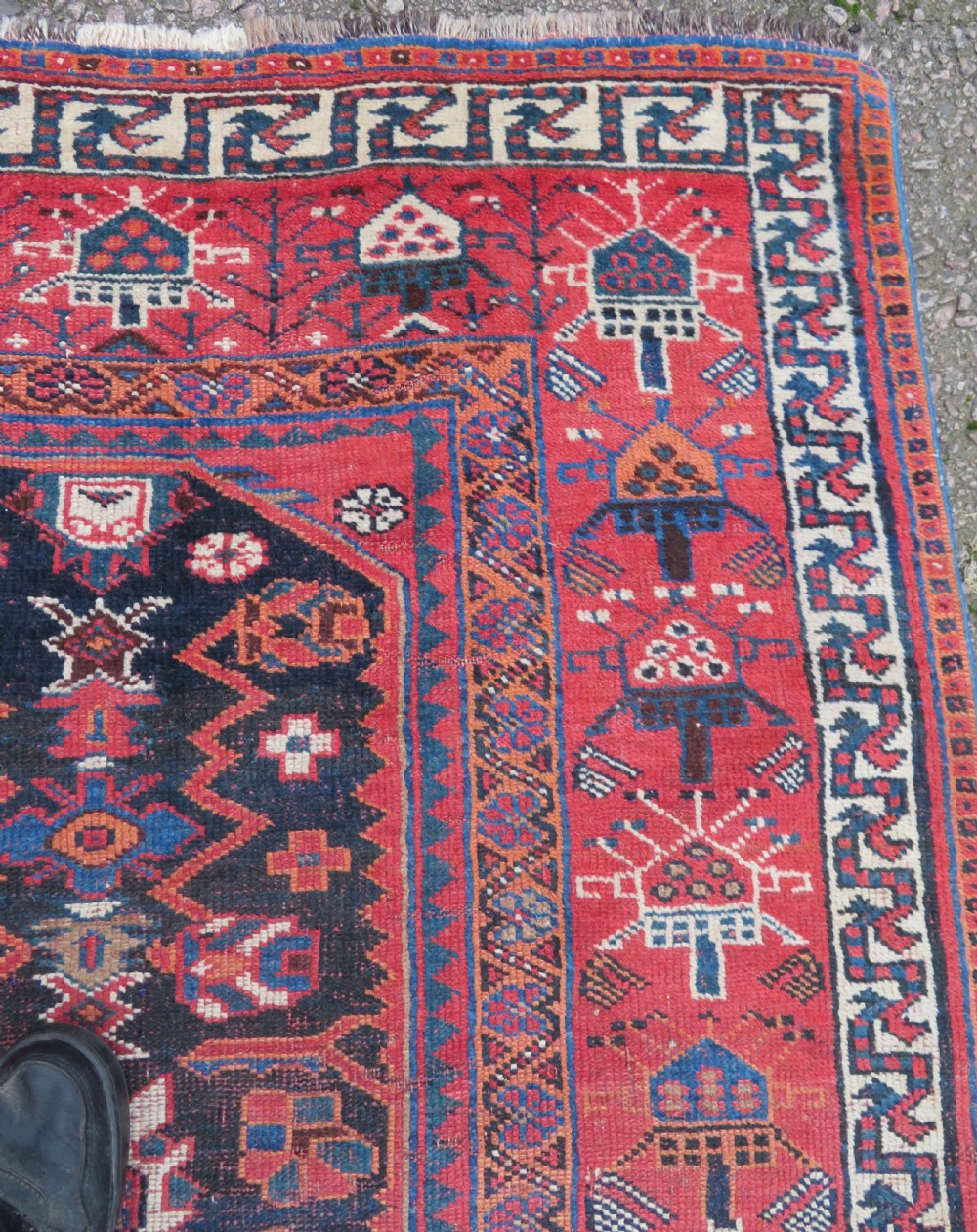 A large hand-knotted Persian Bakhtiari rug featuring geometric diamond medallions on a dark navy field surrounded by a detailed red patterned border. View IX