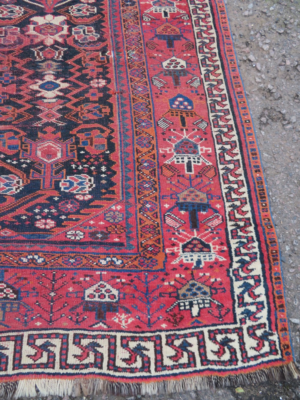 A large hand-knotted Persian Bakhtiari rug featuring geometric diamond medallions on a dark navy field surrounded by a detailed red patterned border. View XI
