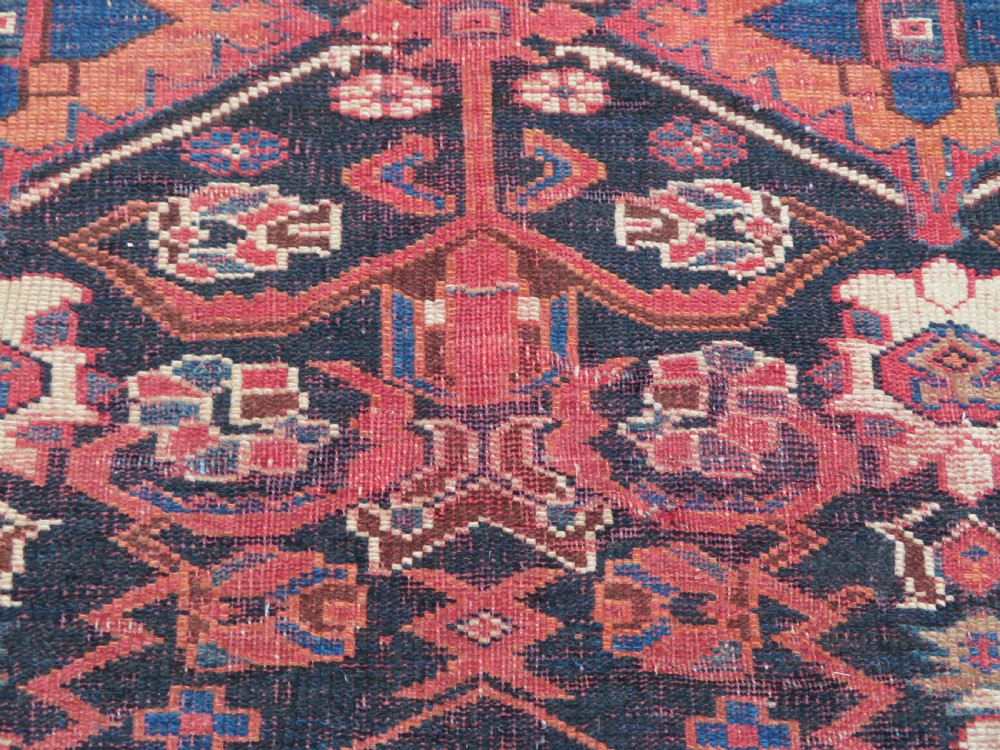 A large hand-knotted Persian Bakhtiari rug featuring geometric diamond medallions on a dark navy field surrounded by a detailed red patterned border. View XIII