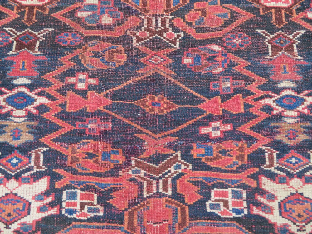A large hand-knotted Persian Bakhtiari rug featuring geometric diamond medallions on a dark navy field surrounded by a detailed red patterned border. View XV